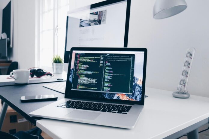 MacBook dengan baris kode di layarnya di meja yang sibuk